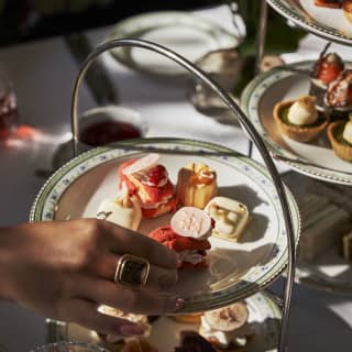 Close-up of a female guest's hand picking a treat from a large afternoon spread of petit-fours, arranged on cake stands.