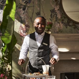 A member of staff smiles broadly as he prepares to clear a table after guests have enjoyed an afternoon tea.
