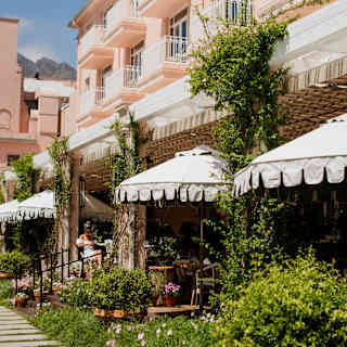 Four white parasols offer additional shade to the awning on the Oasis terrace, filled with potted plants, seen from the path.