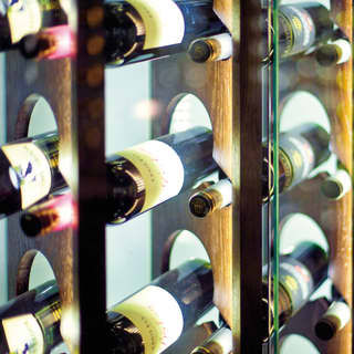 Labelled wine bottles fill a an elegant wooden wine rack, kept behind pristine glass cabinet doors.