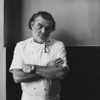 Black and white portrait of Chef Liam Tomlin, arms crossed and serious-faced, with glasses hooked hooked over his collar.