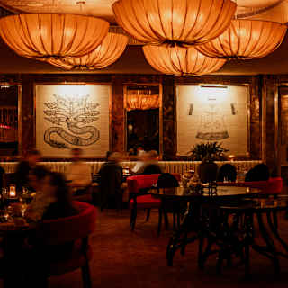 Large orange fabric pendant lights and backlit tapestries create a warm glow for diners, blurred by motion, in the Red Room.