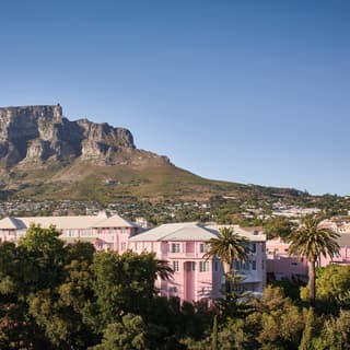 Aerial view of a pink hotel among lush foliage and Table Mountain beyond