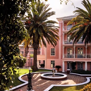 Hotel with pink walls and balconies overlooking palm trees and a fountain
