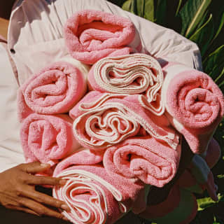 Rolled, pink towels are carried like a giant rose bouquet under the arm of a member of staff in a poolside detail.