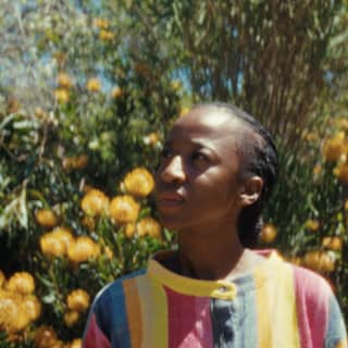 Fashion designer, Sindiso Khumalo stands in a garden with yellow laburnum in one of her playful, rainbow-striped designs.