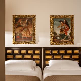 Two Cuzco School religious gilt-framed paintings hang above the wood and gold-tone headboards of Deluxe Room twin beds.