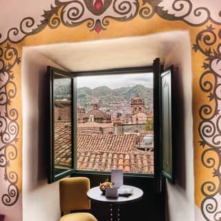 An open junior suite window overlooks the old terracotta roof tops of Cusco with mountains beyond