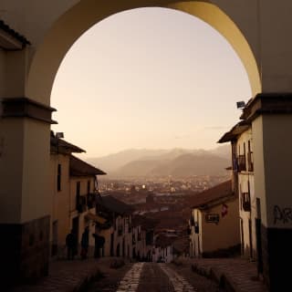 An old cobble road leads under an archway heading towards distant hazy mountains beyond the city