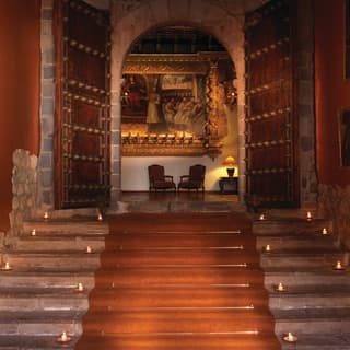 Candlelit stairway leading to open solid-wood doors and an ornate chapel beyond
