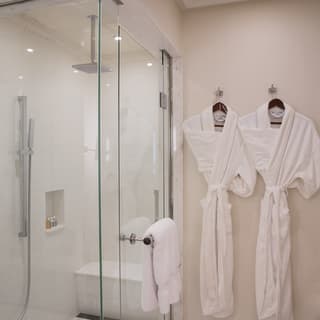 Twin towelling robes hang next to the glass walk-in shower in a luxurious presidential suite