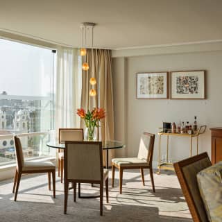 A five-drop light glows above a glass table and chairs by the Limeña Suite window, overlooking Our Lady of Fatima Parish.