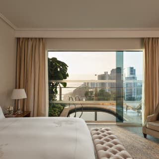 A window looks out onto a private pool and terrace overlooking Lima's coast, seen from the bed inside Limeña Suite.