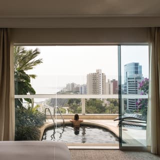 Side-view of a glass wall with a lady relaxing in a balcony plunge pool beyond