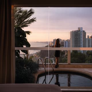 View through glass doors of sunset over Lima reflected in a balcony pool