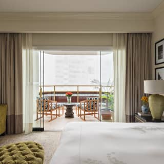 Two chairs on a balcony enjoy a misty city vista, viewed from inside a Terrace Suite over a bed and green velvet furnishings.