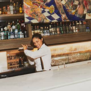 In a white shirt, with tied-back dark hair, mixologist Fiorella Larrea shakes a cocktail at the eclectic Tragaluz bar.