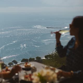 In soft-focus, a woman drinks white wine at an al-fresco table with breathtaking ocean views at the Observatory Restaurant.