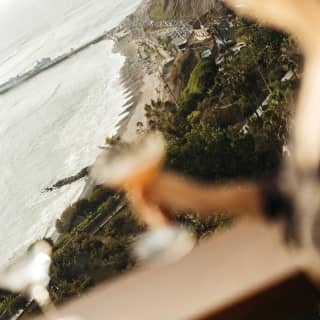 An Observatory guest holds a cocktail in soft-focus, illuminated by sun, as they look out over the dramatic Lima coastline.