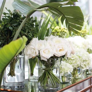 Polished wood side-table covered in vases filled with white roses and peonies