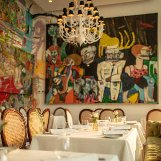 Tables at Tragaluz are embraced by the eclectic flamboyancy of bright wall art by local artists beneath a  Cortez chandelier.