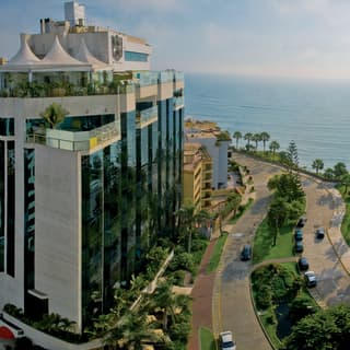 Curved road sweeping past a glass-fronted hotel and the calm ocean at sunset