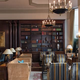 Elegant lamplit hotel lobby with dark wooden bookcase and soft armchairs