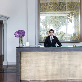 Smiling concierge at a polished concrete desk with a flower arrangement