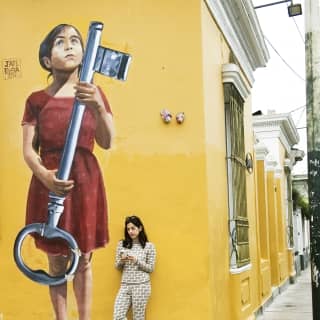 A woman looking at her phone, leaning against a yellow wall in Barranco, Lima