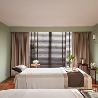 View across the spa treatment room where two beds, with trays of flowers, white sheets and brown satin throws await guests.