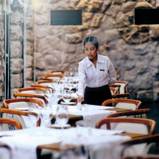A waitress places polished glasses on white-clothed tables lining a wall of full length windows at elegant Tampu Restaurant.