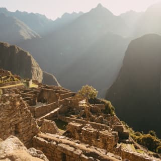 Bright sun blanches the mountain silhouettes in a sweeping view across the ruins of Machu Picchu to the ranges beyond.