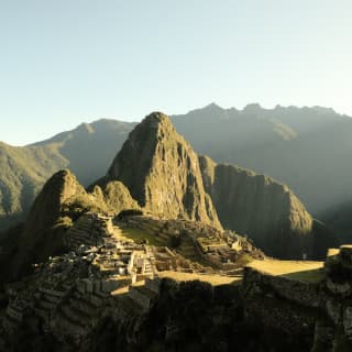 Sunshine illuminates the ancient ruins of Machu Picchu, cradled between the verdant peaks of Huchuy Picchu and Huayna Picchu.