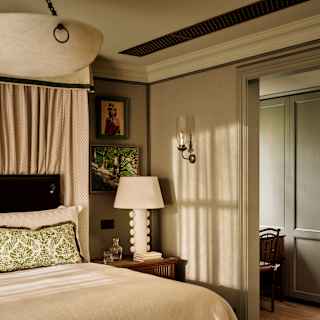 Diagonal view across the Artichoke Suite bed, in beige and green tones with a side table and lamp, to a parallel corridor.