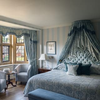 Pale blue tub chairs fill a bay window, framed by blue floral curtains that match the drapes above the bedhead and cushions