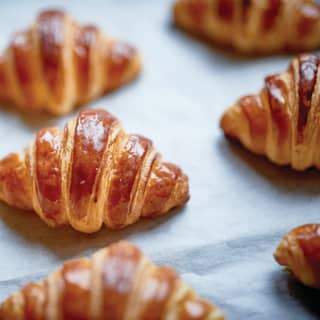 Fresh from the oven, still on baking parchment, is a tray of glistening croissants sitting with the promise of a rich crunch