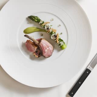 Pink lamb cutlets are artfully arranged on a large white plate with a generous asparagus spear with garnish of petals
