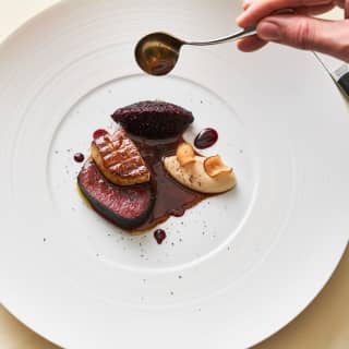 Close-up of a plate of venison with seared duck liver and quenelles of beetroot and creamed potato in a rich meat sauce.