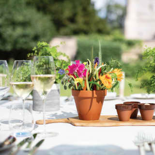 Close-up of a dining table centrepiece with a flowers and vegetable arranged in a clay pot