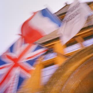 Low-angled, blurred image of the flags of Great Britain, France and Manoir Aux Quatre Saisons flying outside the restaurant.