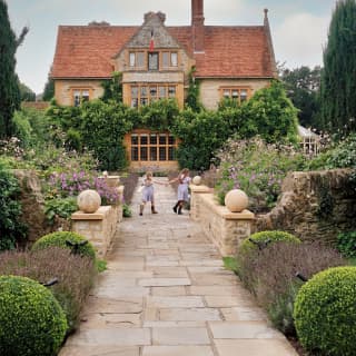 Two young girls in matching blue dresses and wellies, run along a path holding hands as they play in the beautiful gardens