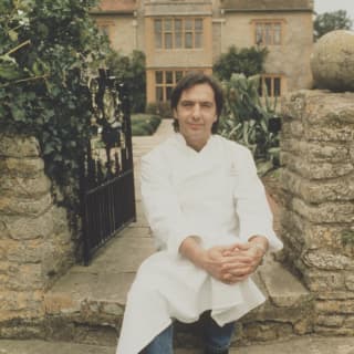 An image of a young dark-haired Chef Raymond Blanc on the garden steps of Le Manoir Aux Quat'Saisons, in jeans and whites.