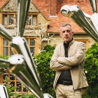 Loris Cecchini stands with arms folded behind his steel sculpture, Arborexence, as it gleams in the greenery of the gardens.