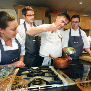 Raymond Blanc demonstrates sugar craft to four people, creating spin sugar baskets by dribbling sugar melt over a ladle