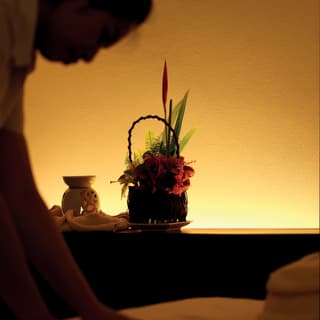Spa staff prepare the white cover of a guest’s treatment table in an atmospheric therapy room