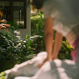 A spa member massages a guest in an outside cabana, seen in soft focus, with garden plants bright in the sunshine.