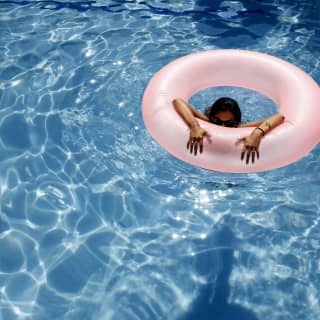 Mujer en una piscina que mira por encima del borde de una dona inflable rosada