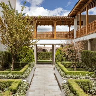 A path cuts through the manicured quad garden with trees boxed by hedgerow dividers and overlooked by colonnades and loggias.