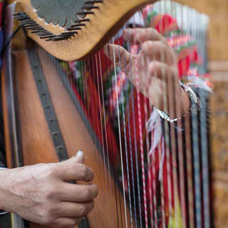 Close-up of two hands playing a wooden carved harp
