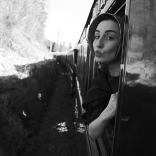 A woman in an Audrey Hepburn headscarf puckers her lips to offer a kiss as she leans out the window of the carriage